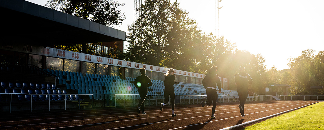 Ungdomar springer på en friidrottsarena i motljus